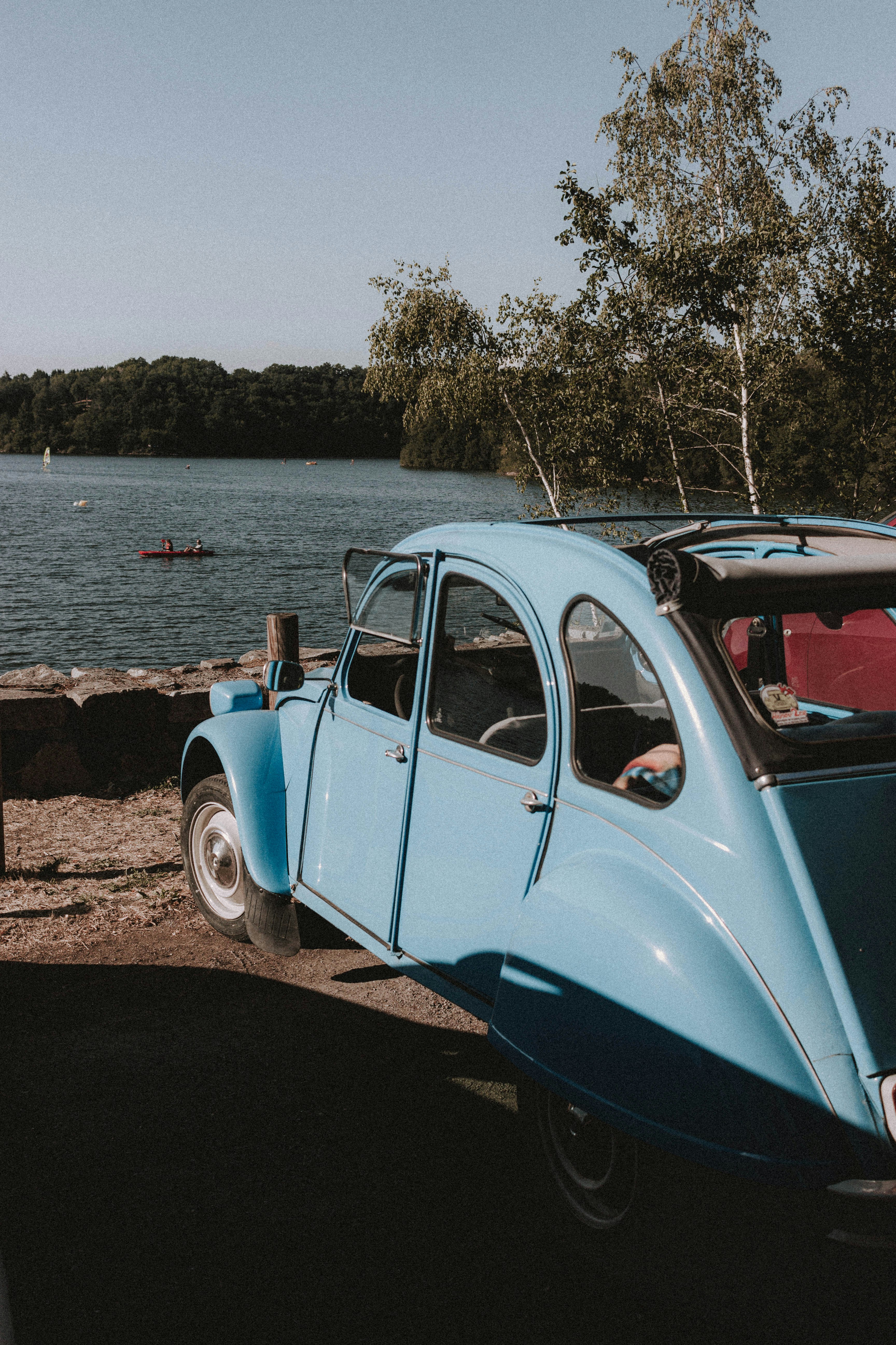 blue and white vintage car parked beside body of water during daytime